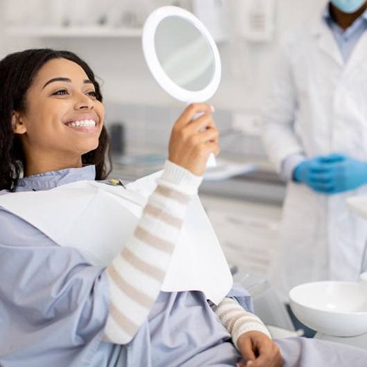 Happy dental patient looking at her smile in the mirror