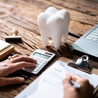 Hands calculating invoice at wooden desk with large model tooth