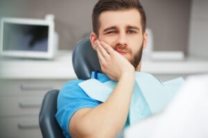 Patient sitting in dentist’s chair holding side of face in pain.